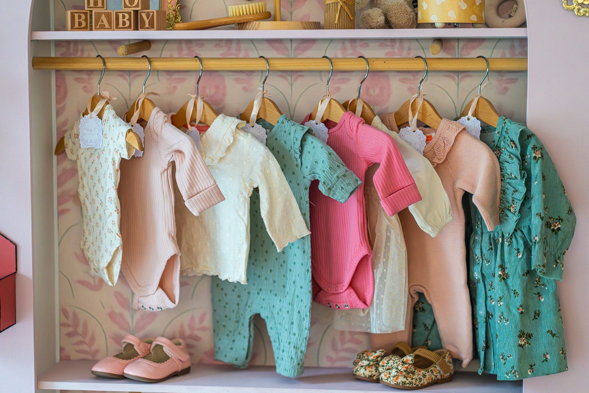 Babywear hanging on a rail above small shoes